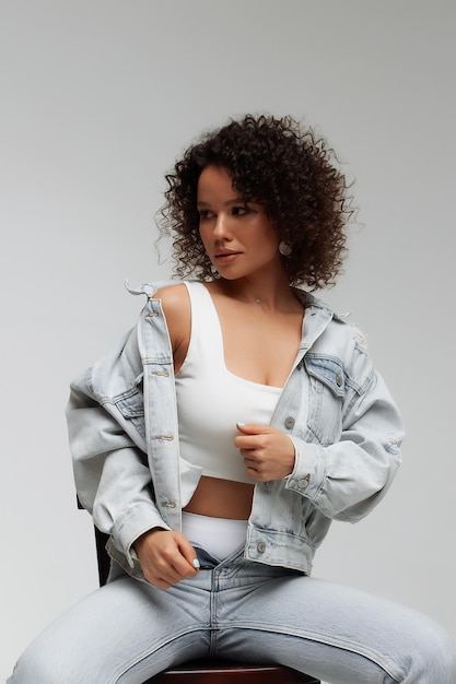 Full body of confident young barefoot female model with curly hairstyle wearing trendy denim jacket