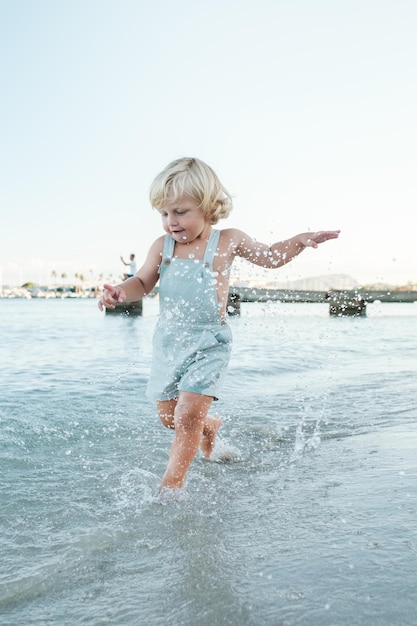 Full body of cute little toddler playing and running in rippling sea on sunny summer day