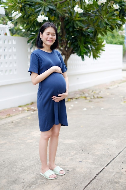 Full body een zwangere moeder in een lange blauwe jurk staat in de tuin