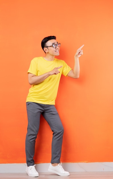 Full body foto van Aziatische man in geel shirt op oranje muur