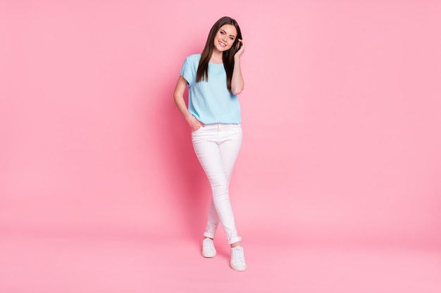 Full body foto van charmante jonge dame goed humeur draag blauw t-shirt witte broek sneakers geïsoleerde roze kleur achtergrond