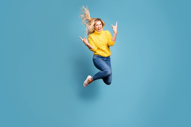 Full body foto van gekke dame hoog springen genieten van metal rock concert tonen handen hoorns opgewonden slijtage gebreide gele trui jeans geïsoleerde blauwe kleur muur