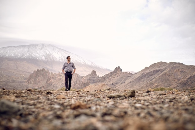 Full body ground level of Hispanic male traveler admiring picturesque view of mountain Teide covered with snow while traveling in Tenerife Canary Islands Spain