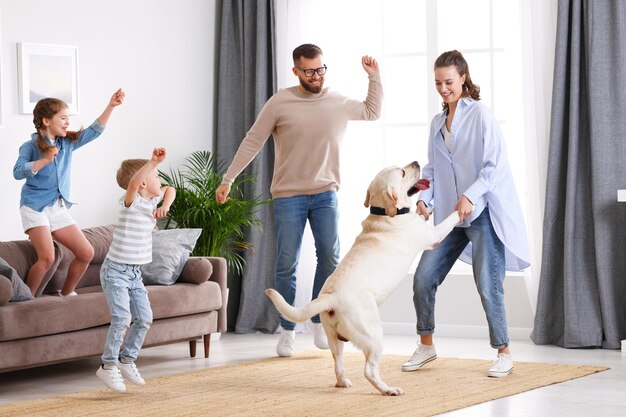 Full body of happy playful family parents and little kids with\
cute purebred labrador retriever dog having fun and dancing\
together in living room at home