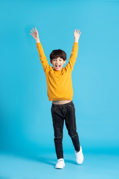 Полное изображение азиатского мальчика, позирующего на синем фоне