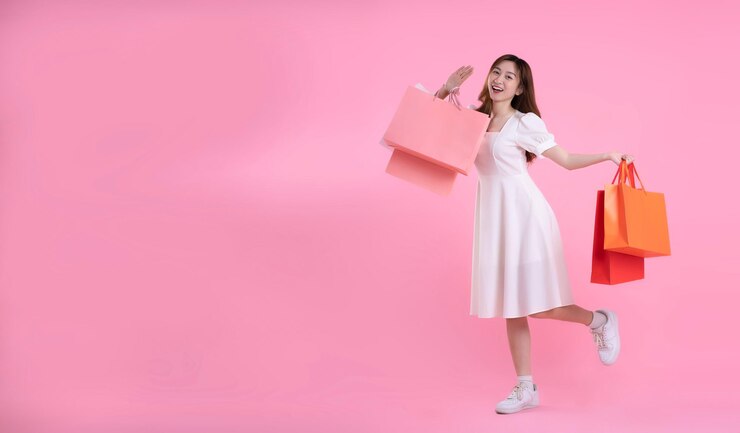 Photo 쇼핑백을 들고 분홍색 배경에 포즈를 취하는 아시아 여성의 전신 이미지