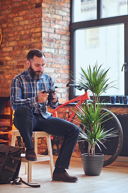 The full body image of a bearded hipster amateur photographer taking pictures in a room with loft interior