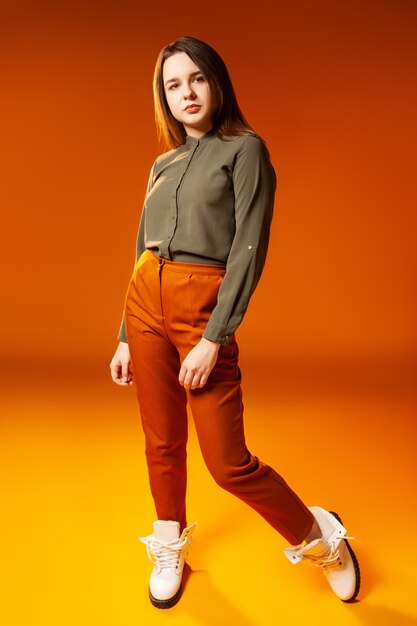 Full body jonge vrouwelijke model in stijlvolle casual kleding camera kijken tegen oranje achtergrond