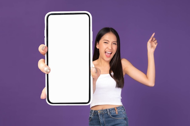 Ritratto di foto a figura intera di bella giovane donna asiatica ragazza sorpresa eccitata che mostra un grande smartphone con schermo bianco a schermo vuoto isolato su sfondo viola mock up image