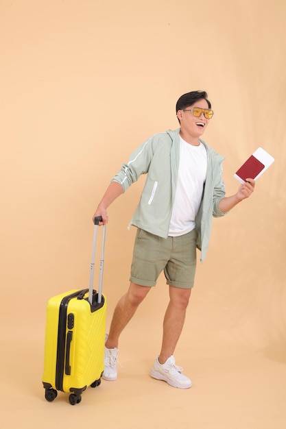 Full body length of a young handsome happy cheerful Asian male adult man, with yellow luggage.