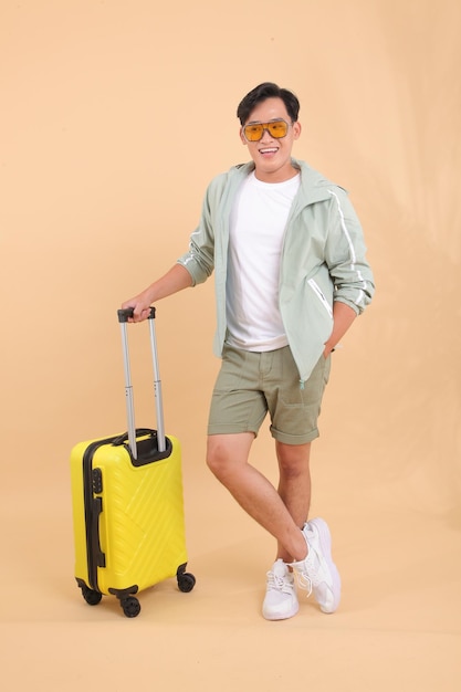 Full body length of a young handsome happy cheerful Asian male adult man, with yellow luggage.