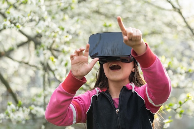 Full body little girl excited and entertained, playing with virtual reality glasses, exploring a fantasy world, trying to touch something.