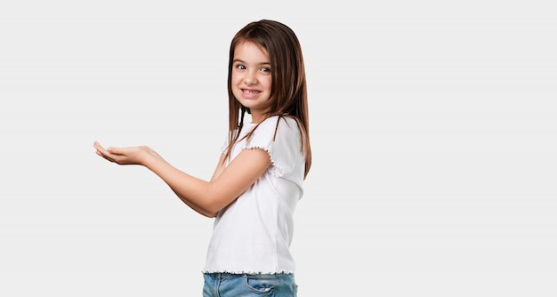 Photo full body little girl holding something with hands, showing a product, smiling and cheerful