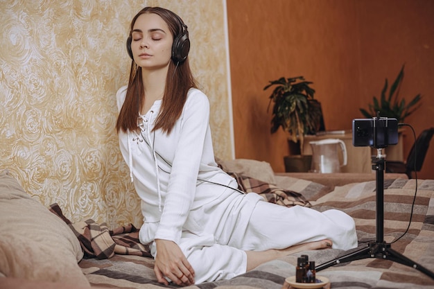Фото Полное тело спокойной женщины в наушниках, практикующей йогу во время онлайн-урока по телефону дома