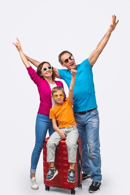 Full body parents and son gesturing with hands while gathering around suitcase before journey against white background