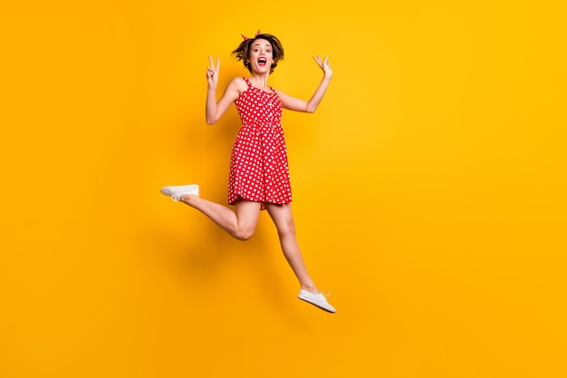 Full body photo of cheerful enthusiastic girl jump enjoy spring free time holiday make v-sign wear good look retro style skirt footwear isolated over shine color wall
