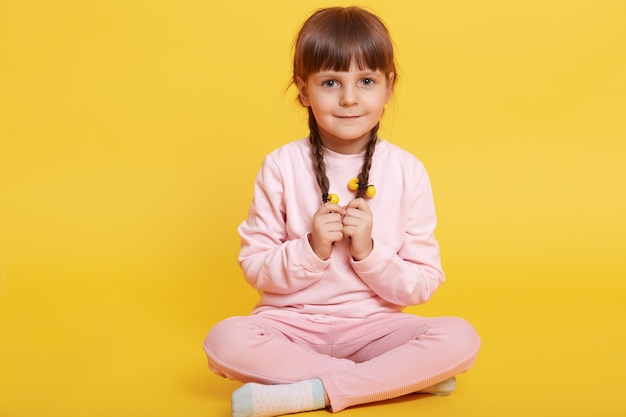 Full body photo of coy kid sitting with crossed legs