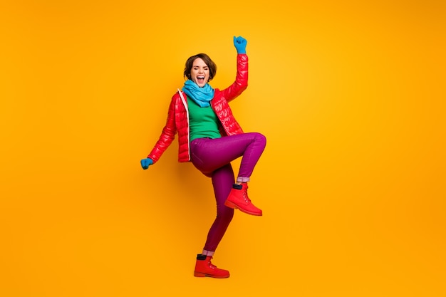 Full body photo of funky excited lady raise hands leg ecstatic expression wear casual red coat blue scarf gloves green turtleneck trousers footwear 