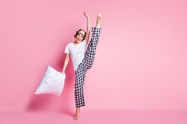 Full body photo of funny lady hold pillow raise leg on pink wall