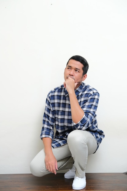 Photo full body portrait of adult asian man showing thinking gesture on knee