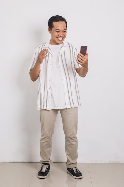 Full body portrait of asian man smiling happy looking at mobile isolated on white background