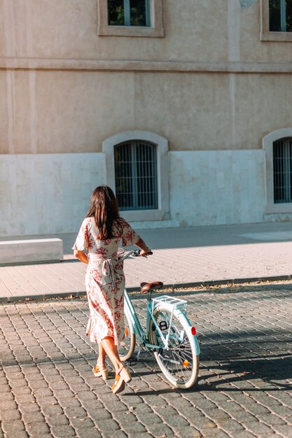 屋外でレトロな自転車と立っているコートに身を包んだ美しいスタイリッシュな女性の全身の肖像画