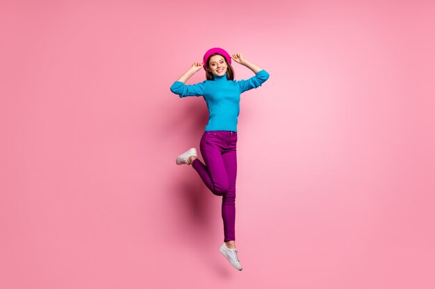 Full body portrait of charming cheerful girl jump enjoy weekends touch her modern french beret feel content emotions wear stylish clothes.