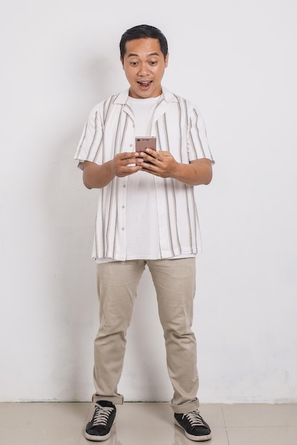 Full body portrait of cheerful asian man and get surprise when looking at cell phone