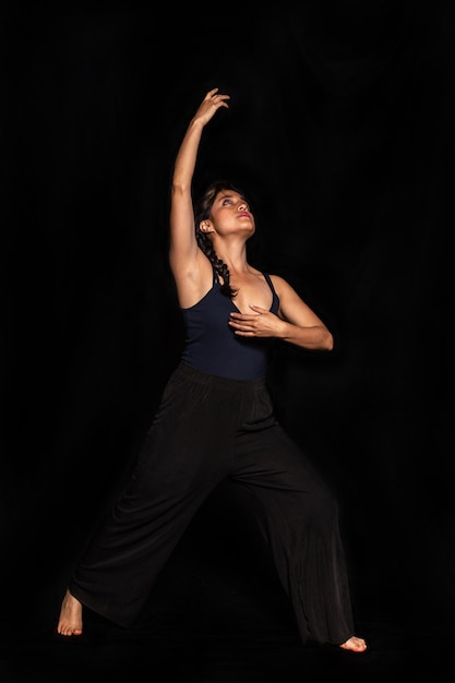 Full body portrait of a Latin woman posing isolated on black background looking and stretching her arm up Female body expression concept