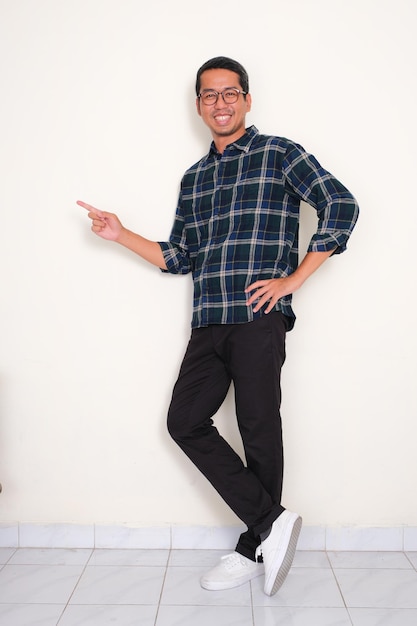 Photo full body portrait of a man standing and pointing to the right side with happy expression