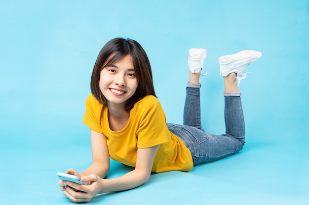 Full body portrait of playful asian girl lying on blue background