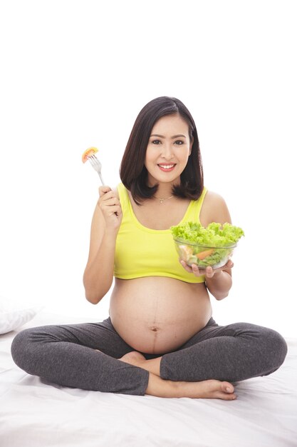 Full body portrait of pregnant woman holding a bowl of healthy salad