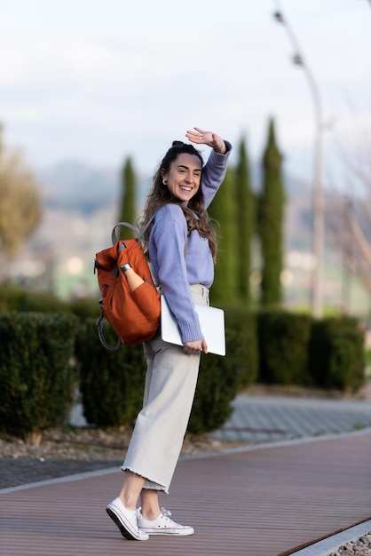 Ritratto completo del corpo di una graziosa imprenditrice che guarda indietro e saluta con la mano in un parco.