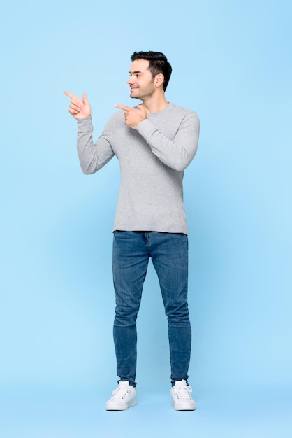 Full body portrait of smiling cheerful young handsome Caucasian man in casual clothes pointing hands aside on light blue background