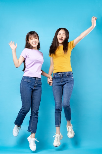 Full body portrait of two beautiful young Asian girls on a blue wall