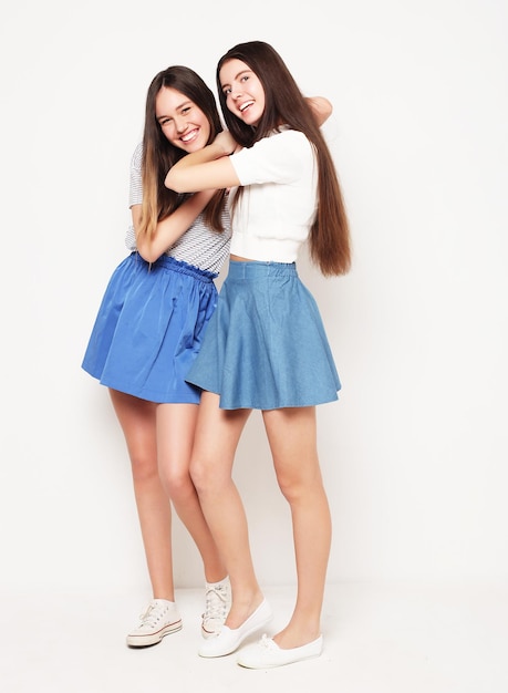 Full body portrait of two happy girls wearing blue skirts over white background