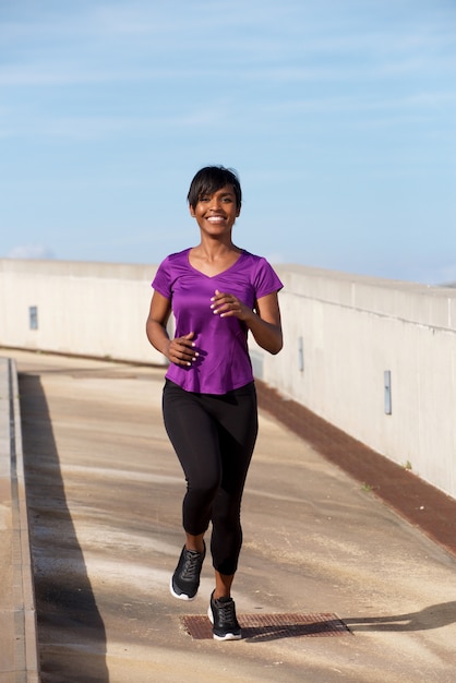 Full body portrait young black woman jogging outdoors and smiling