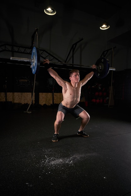 Полное тело профессионального мускулистого спортсмена-мужчины, поднимающего тяжелую штангу с гирями над головой во время тренировки в тренажерном зале