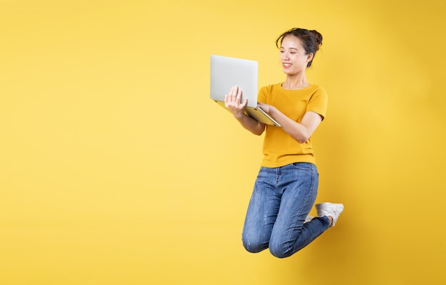 Full body profile photo of young asian girl jumping high holding a laptop writing a new social media post, isolated on blue background