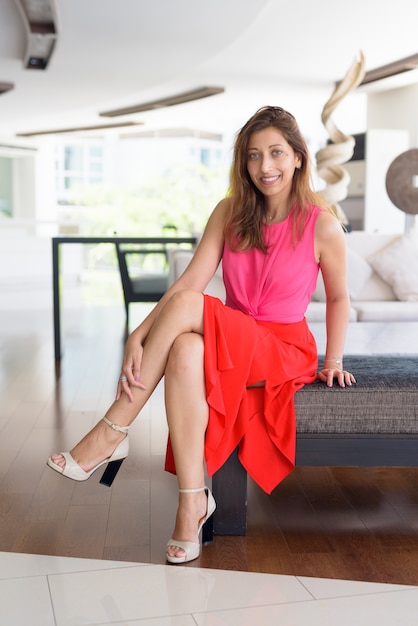 Full body shot of happy beautiful Hispanic woman sitting at home indoors