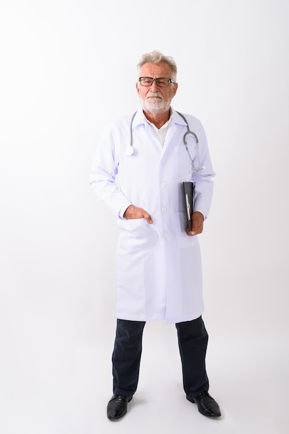 Full body shot van knappe senior bebaarde man arts staande terwijl klembord op wit