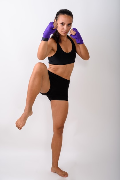 Full body shot of young Asian woman fighter with leg raised ready to fight against white space