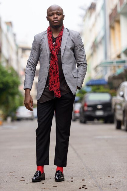 Full body shot of young bald African businessman with scarf outdoors