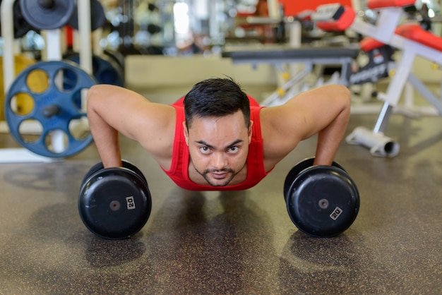 Foto colpo di corpo pieno di giovane uomo indiano barbuto facendo push up con manubri