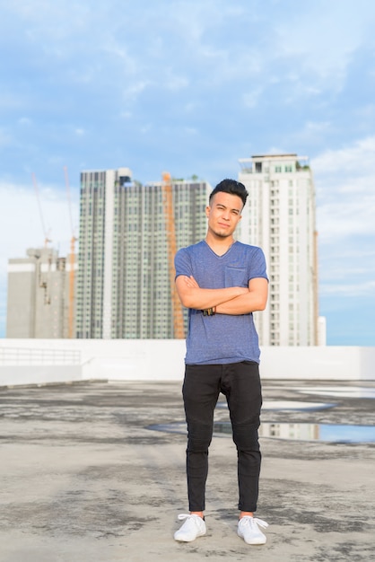 Full body shot of young handsome multi ethnic man with arms crossed against view of the city