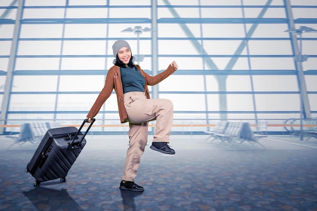 空港でスーツケースを運ぶ満面の笑みを浮かべた若い旅行者のアジアの若い女性の全身側面図