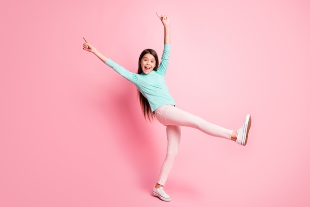 Foto a grandezza naturale di carina graziosa signora ispanica lunga acconciatura danza alzare le mani in alto le dita dirette indossare pantaloni felpa turchese scarpe da ginnastica bianche isolate sfondo di colore rosa