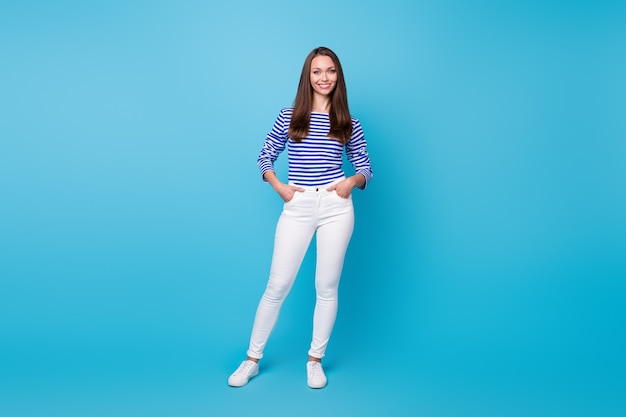 Full body size photo of pretty young girl slim figure hands pockets businesswoman vacation concept wear striped shirt white trousers sneakers isolated vivid blue color background