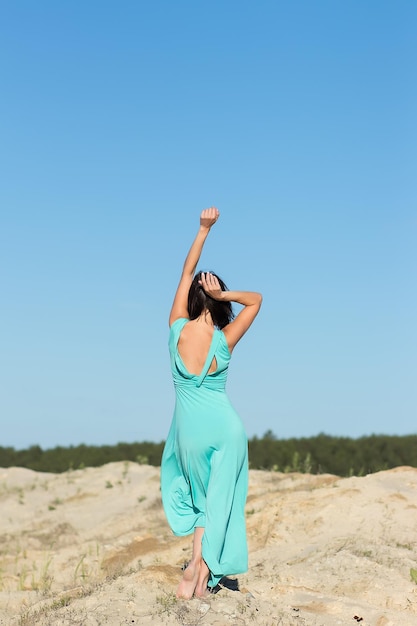 Full body slanke sensuele vrouw met vliegend haar in lange turquoise jurk terwijl ze in de wind aan de kust staat