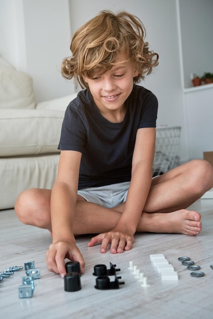 Photo full body of smiling boy sorting fasteners and assembling furniture sitting on floor in cozy living room at home